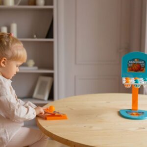Young girl enjoying a fun indoor activity with a mini basketball hoop toy on a table.