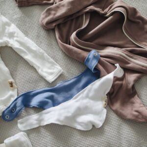 From above of small cotton suits and bibs for little babies on gray waffle bedspread on bed at home on daylight