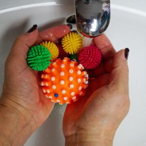 Hands holding colorful rubber balls under running water in a sink, perfect for toy washing themes.