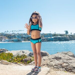 A young girl stands confidently on the rocky beach, enjoying a sunny day by the ocean.