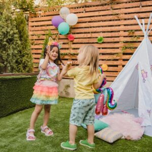 Two children play joyfully with balloons near a teepee tent, enjoying an outdoor party setting.