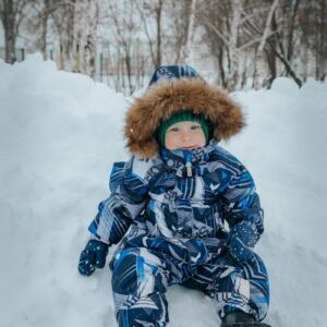 a small child sitting in the snow wearing a snow suit