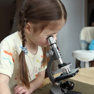 A young girl looks intently into a microscope.